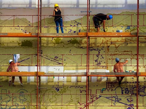 Workers on scaffolding paint a vibrant mural, showcasing collaboration and artistry.